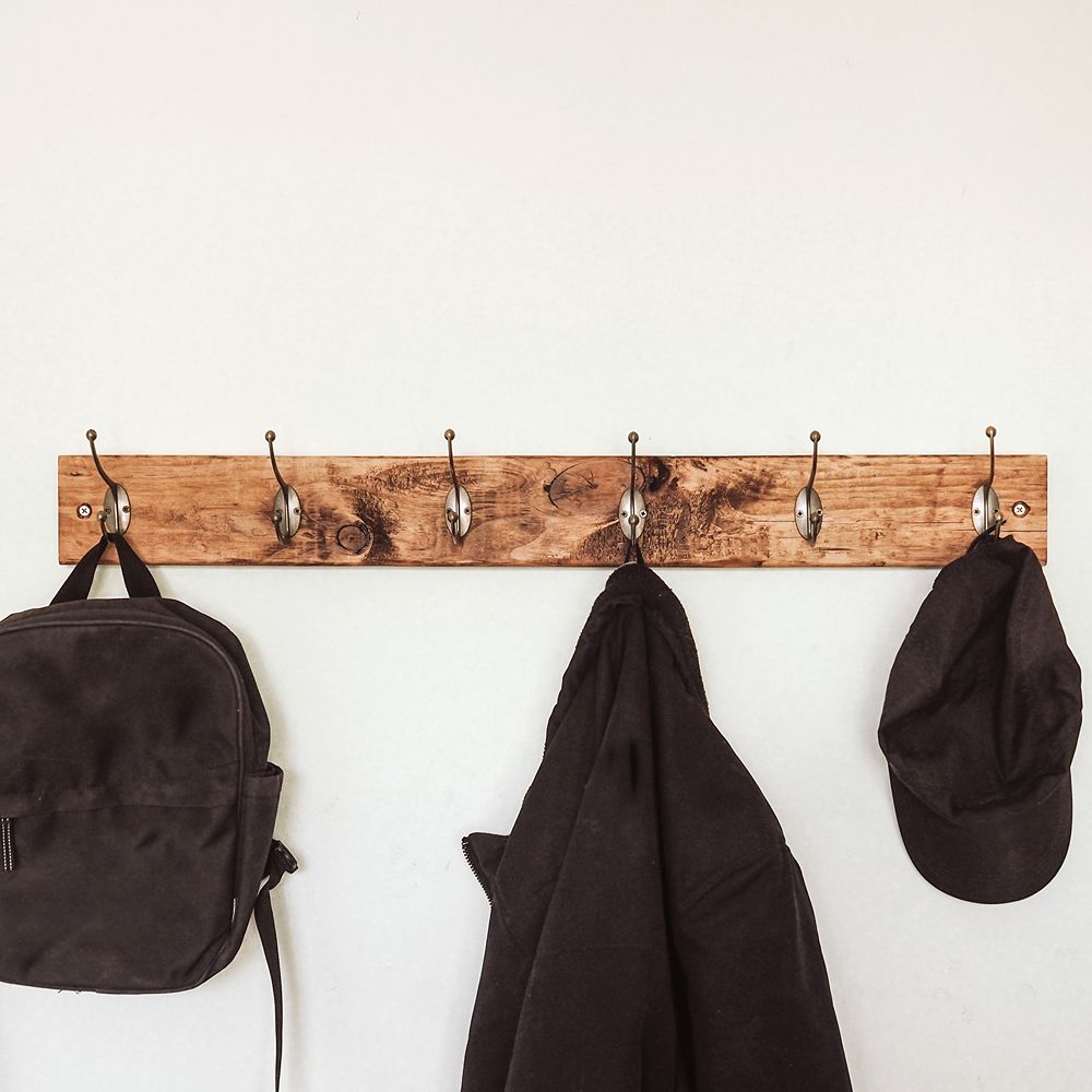 Wooden coat rack with hooks holding a backpack, jacket, and cap against a white wall.