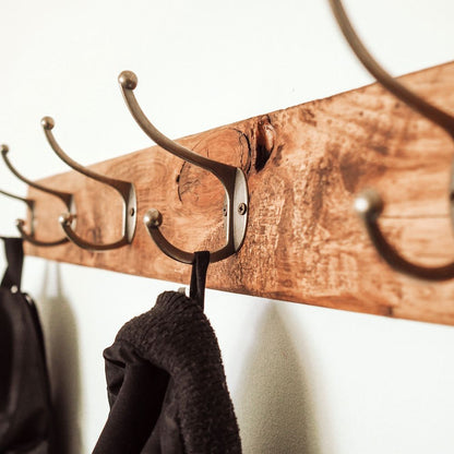 Wooden coat rack with metal hooks on a white wall, with clothes hanging from it.