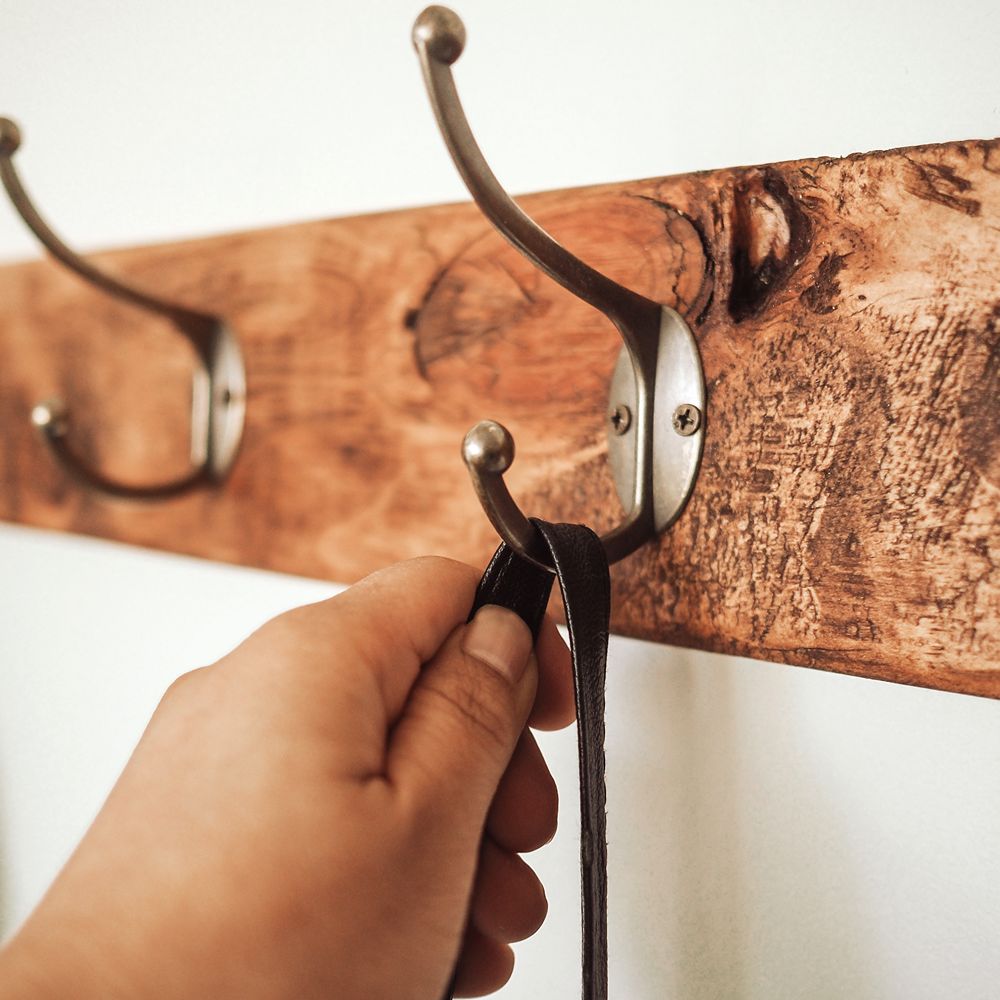 Hand trying to hang on a double hook wooden coat rack with three hooks.
