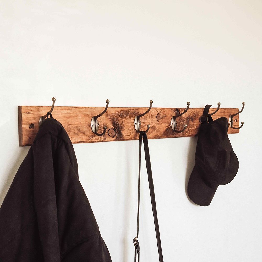 Wooden coat rack with hooks holding a black coat, black bag, and black sock against a white wall.