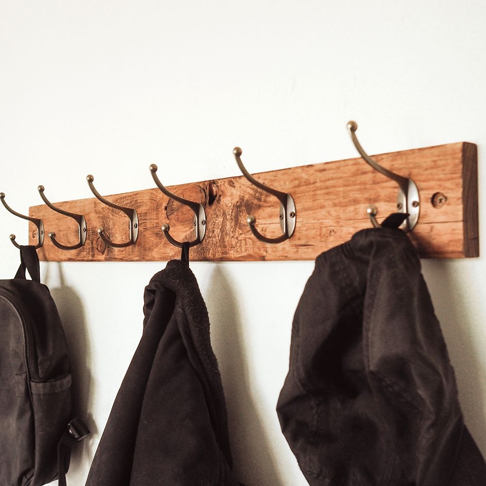 Wooden coat rack with hooks holding coats against a white wall