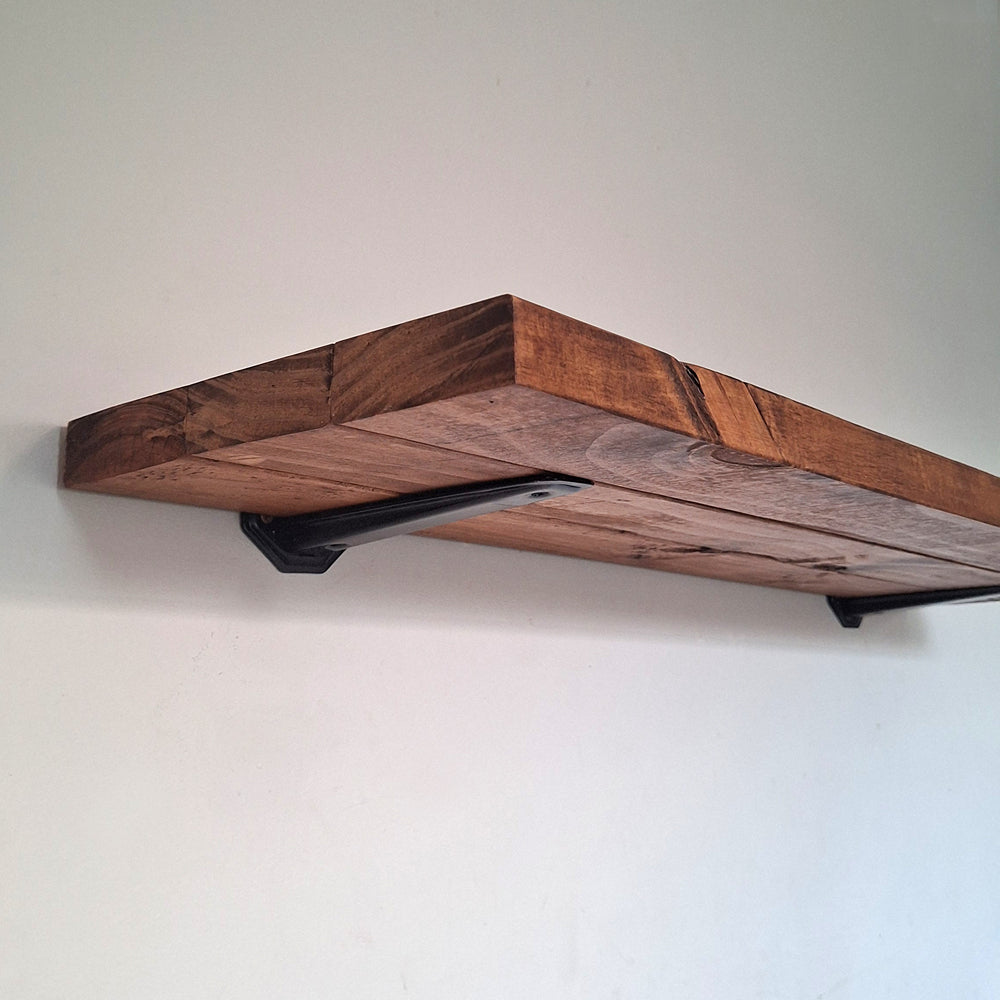 Underneath close-up view of a handcrafted walnut brown pine wood shelf showcasing the heavy-duty black mounting bracket and organic wood grain.
