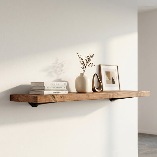 Long farmhouse style timber floating shelf in walnut brown styled with minimalist books, a modern white vase, and a gold photo frame in a bright living space.