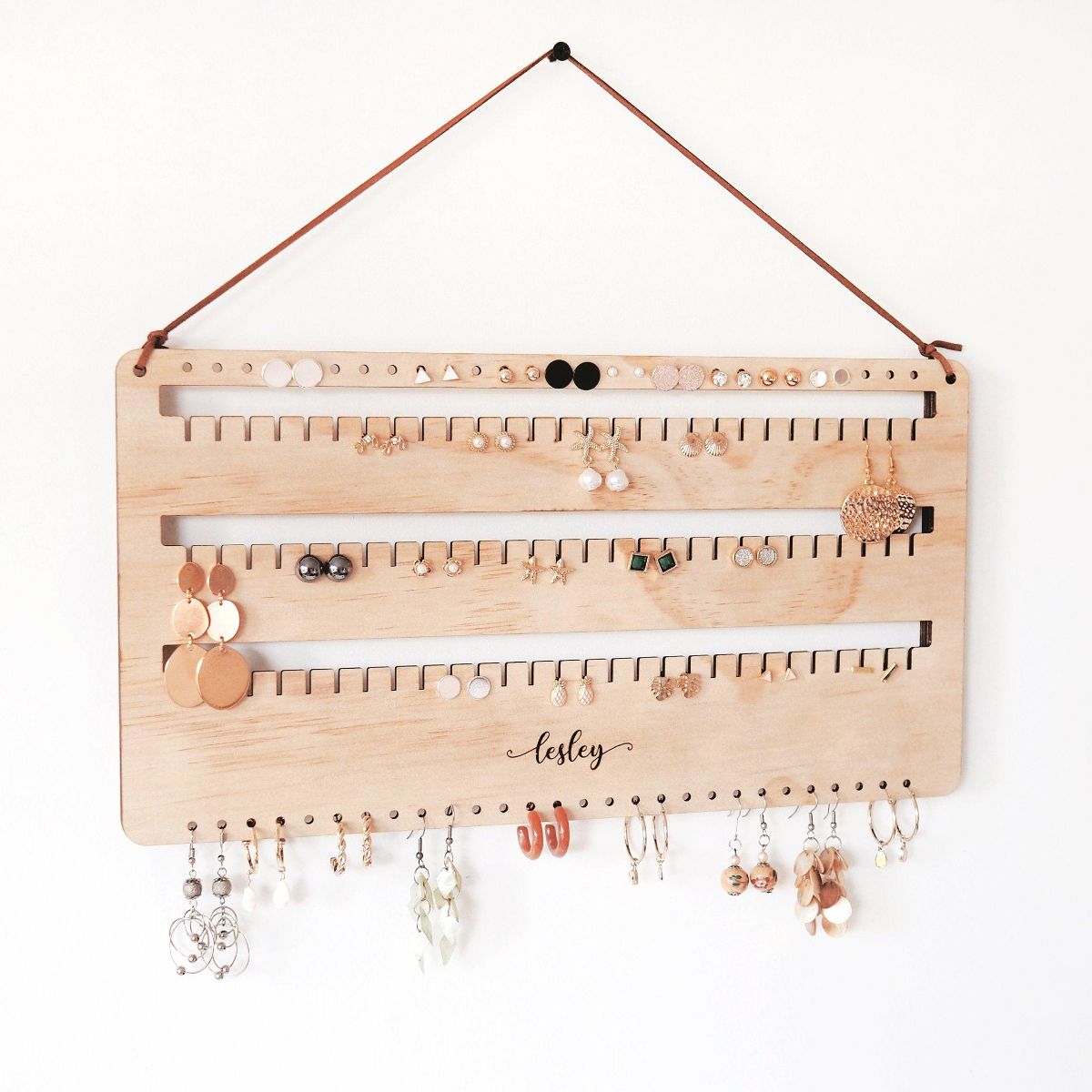 Right side view of a personalised wall earring holder with leather string hanging on a screw. Stud, hook and dangling earrings are organised on this earring holder. A perfect gift for mum