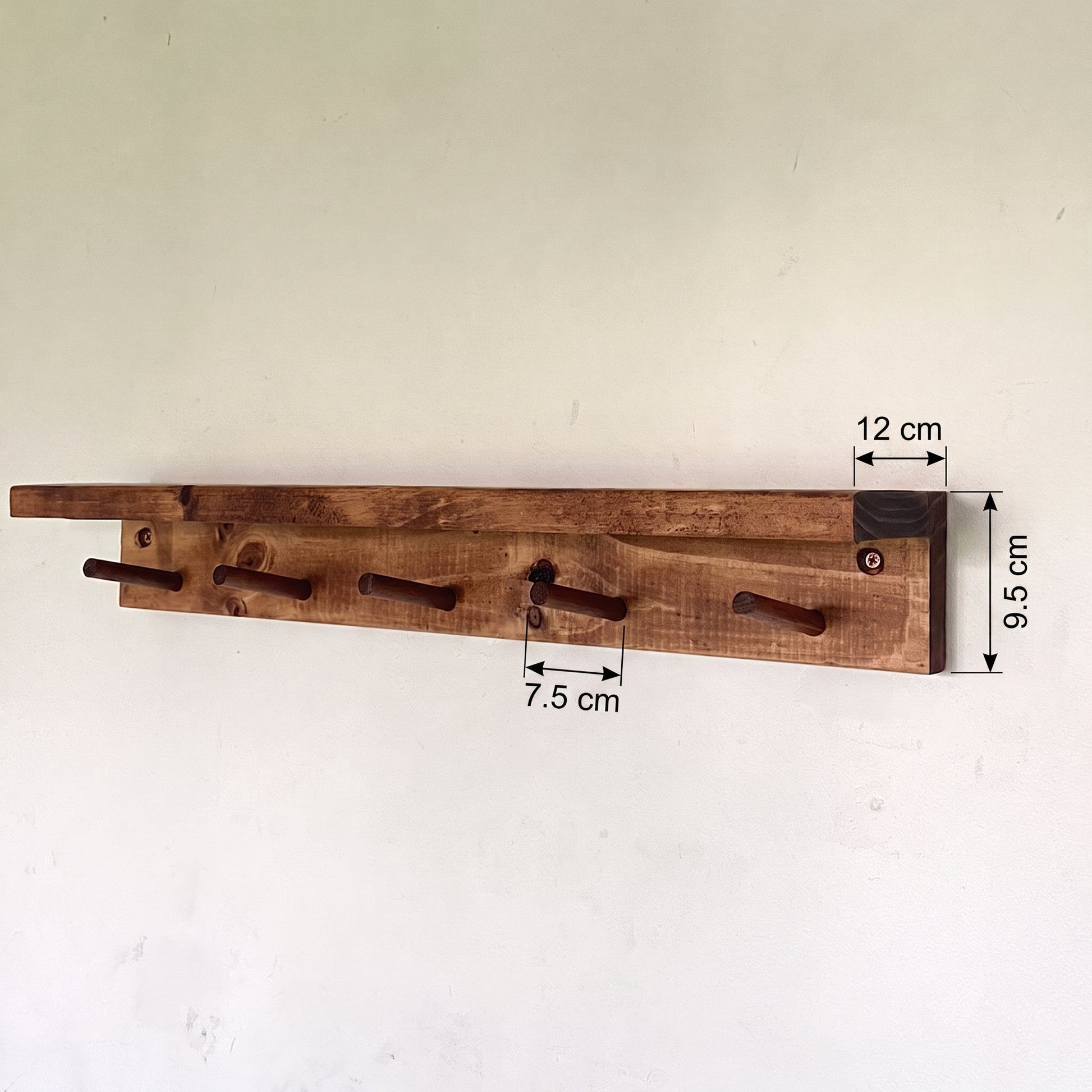 A rustic wooden wall-mounted coat rack with five hooks, shown against a plain off-white wall with dimension annotations indicating 9.5 cm height, 12 cm hook width, and 7.